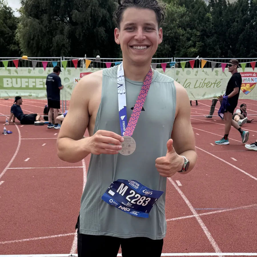 Anthony on the track after a marathon finish, holding his medal, thumbs up